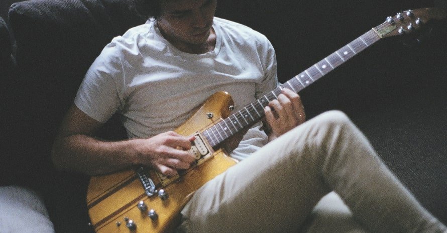 A man sitting down to play the electric guitar